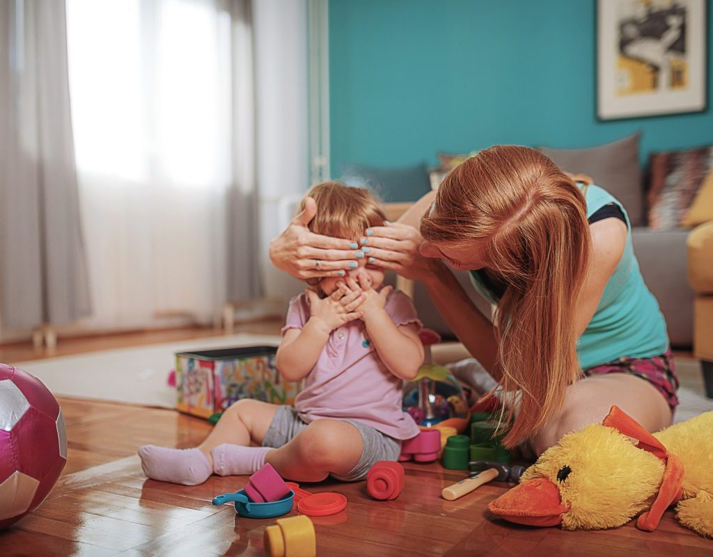 Mother playing peekaboo with her small child.