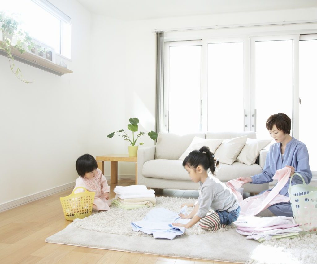 A mother and two young children folding laundry on the living room floor