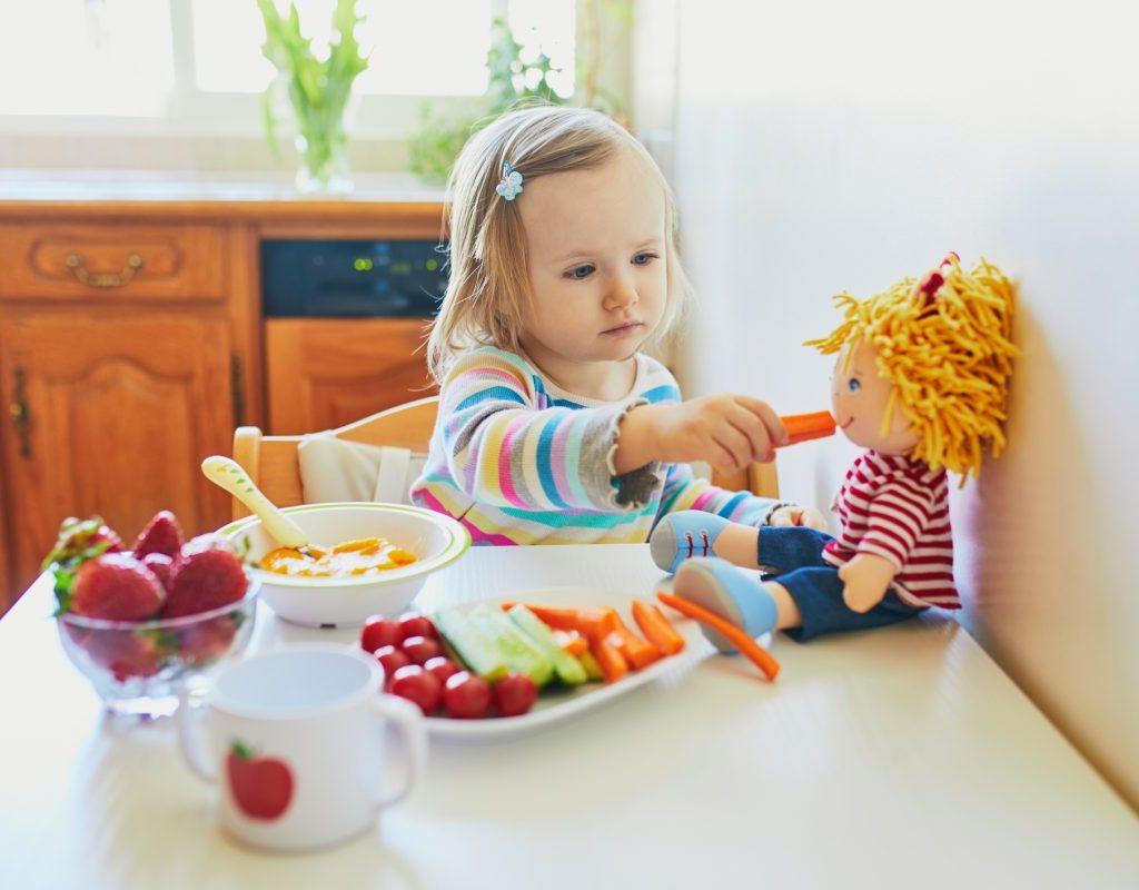 A little girl feeding her food to her toy