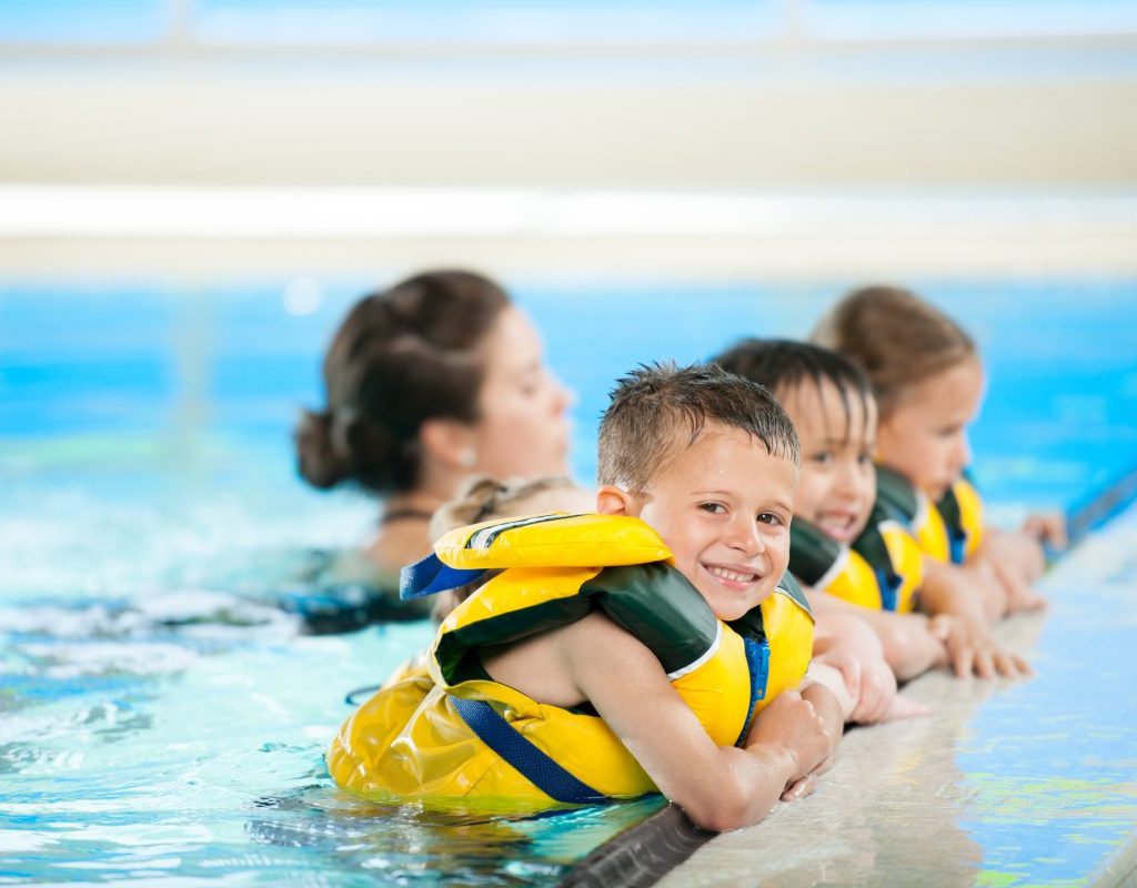 A group of young kids wearing life jackets getting ready to start a swim lesson