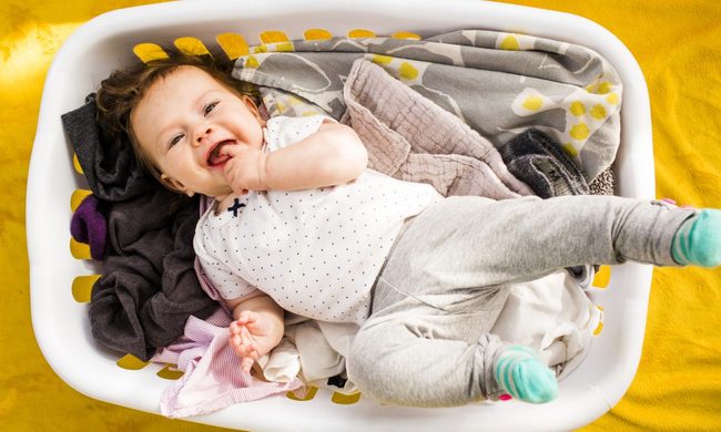 A baby on top of clothes in a laundry basket