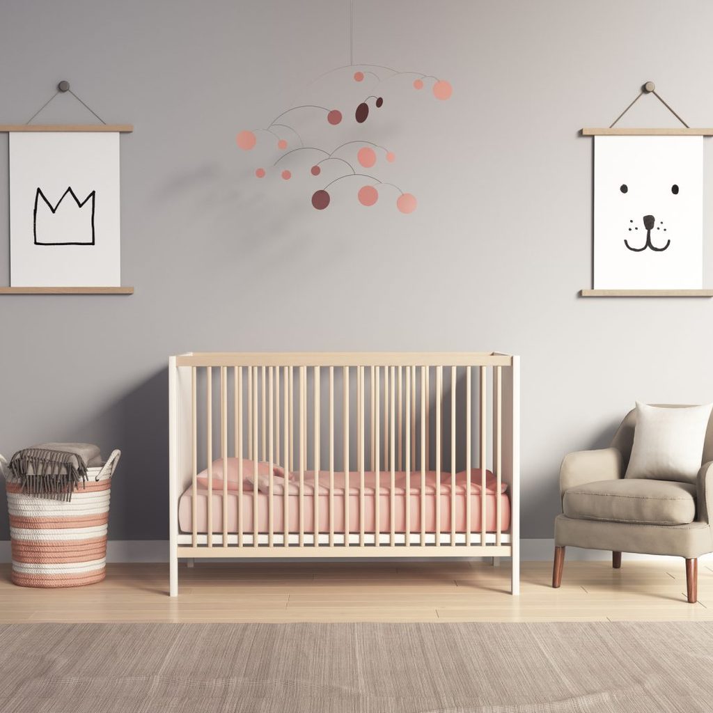 A baby nursery with a crib, chair, wall hangings, and laundry basket