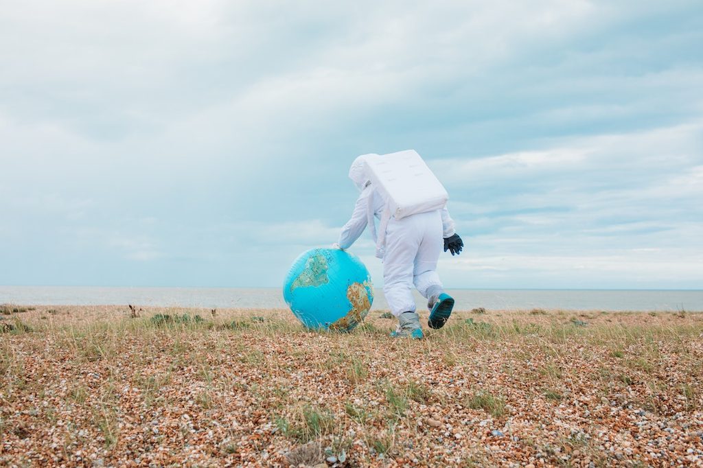 Person wearing astronaut costume pushing a globe