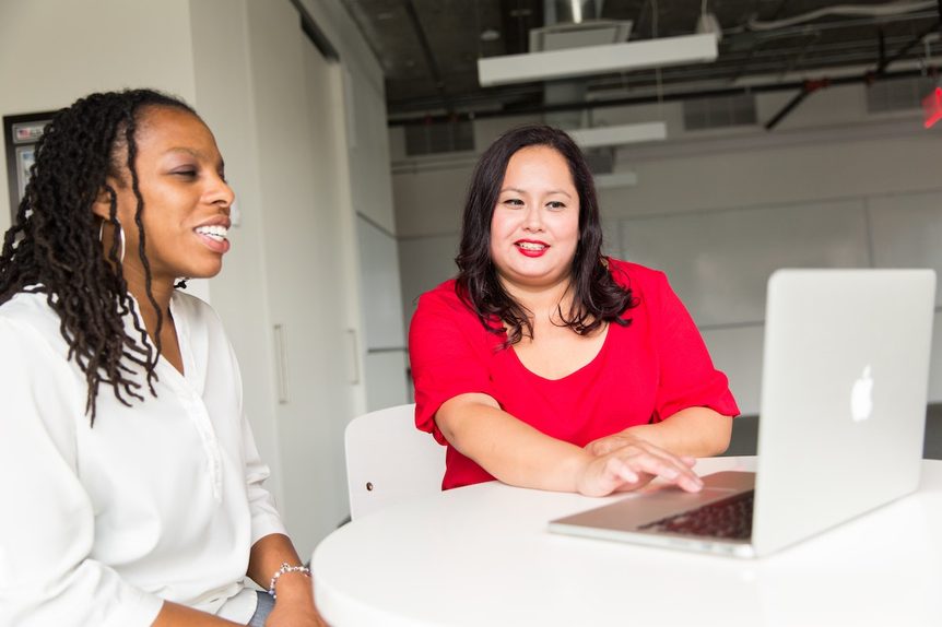 Two women sitting in front of computer smiling