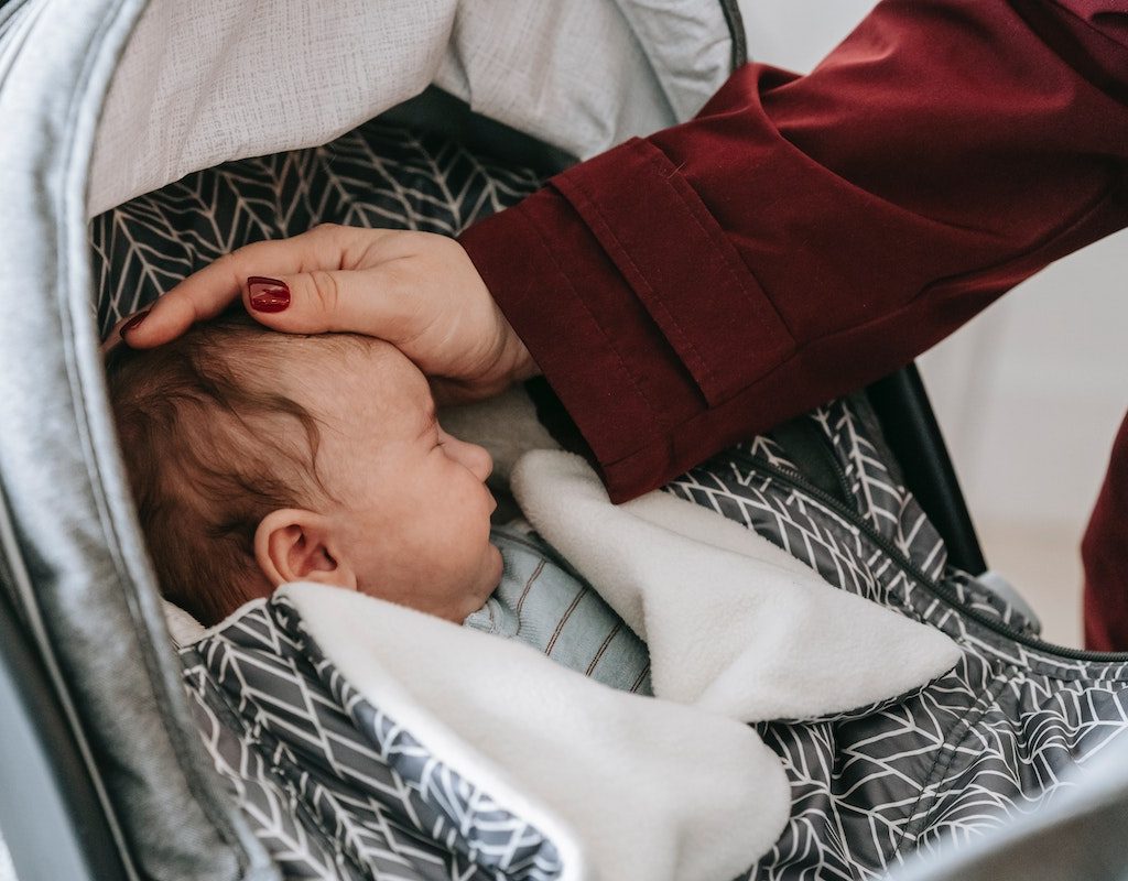 Newborn asleep in stroller with mom patting head