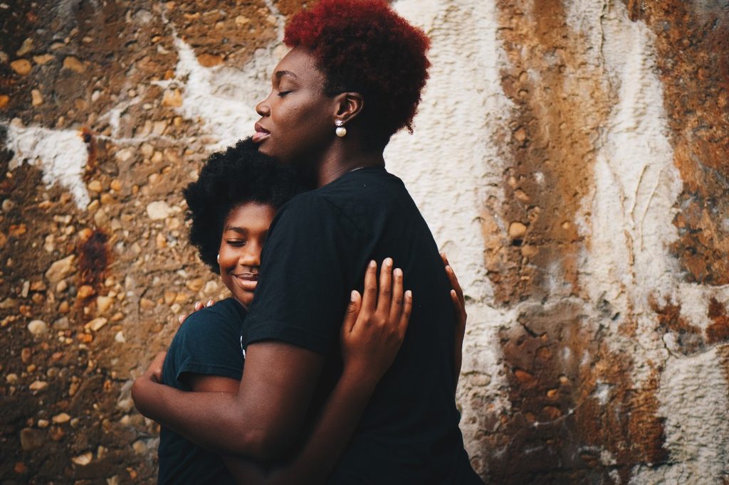 Adult hugging a teenager in front of a wall