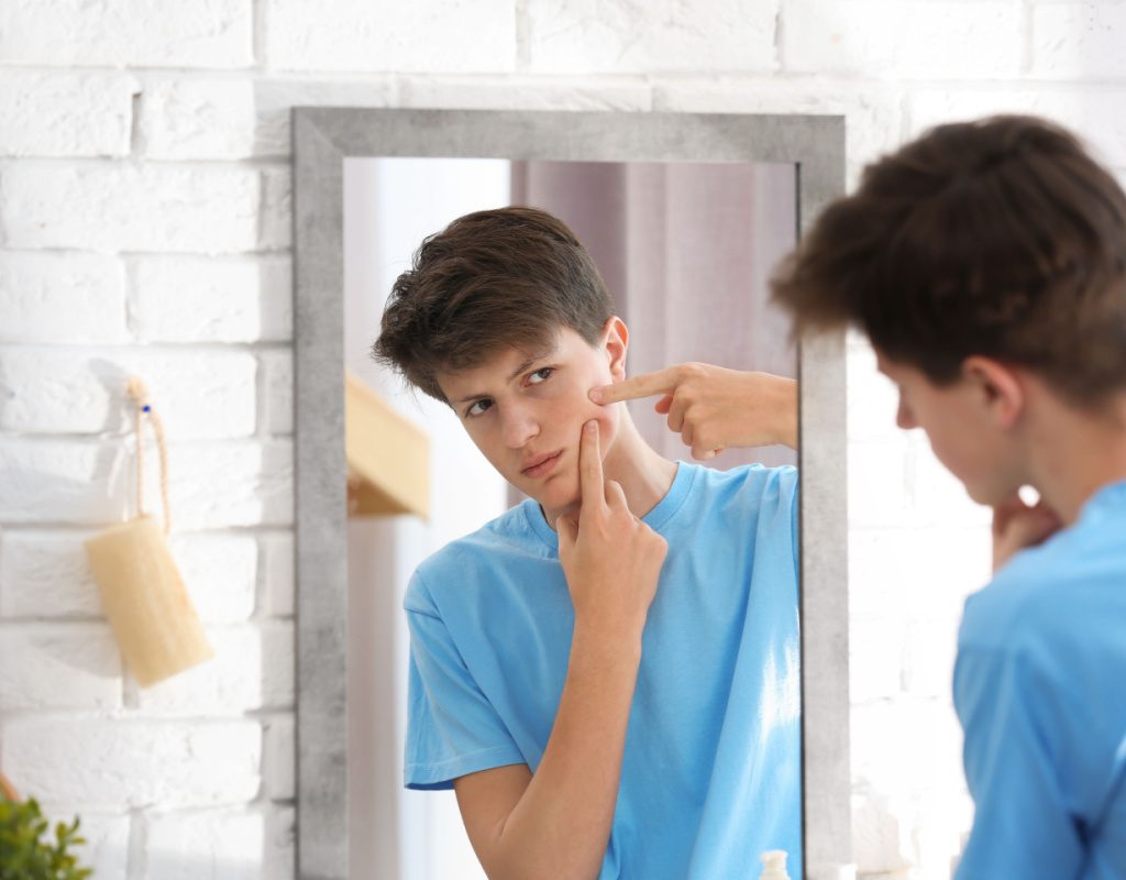 Teen boy looking in the mirror and trying to pop a pimple
