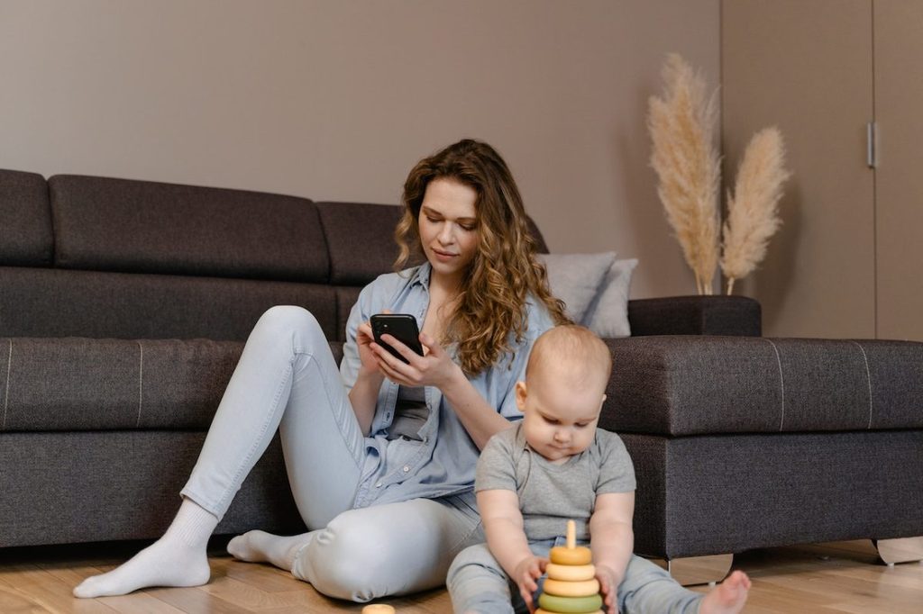 A mother on her phone while a baby plays in front of her