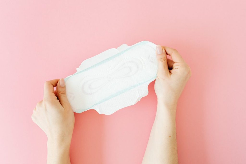 A menstrual pad being held on a pink background