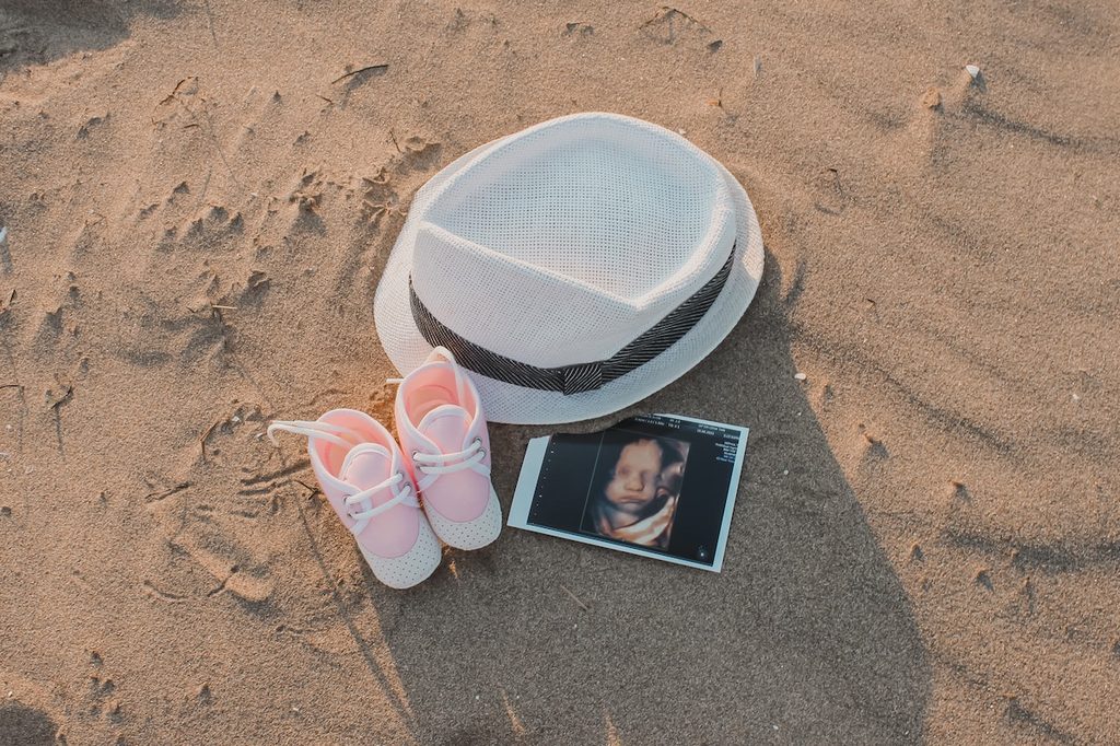 3D sonogram with hat and pink shoes in sand
