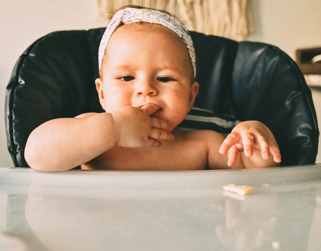 A baby sitting in a high chair with their finger in their mouth.