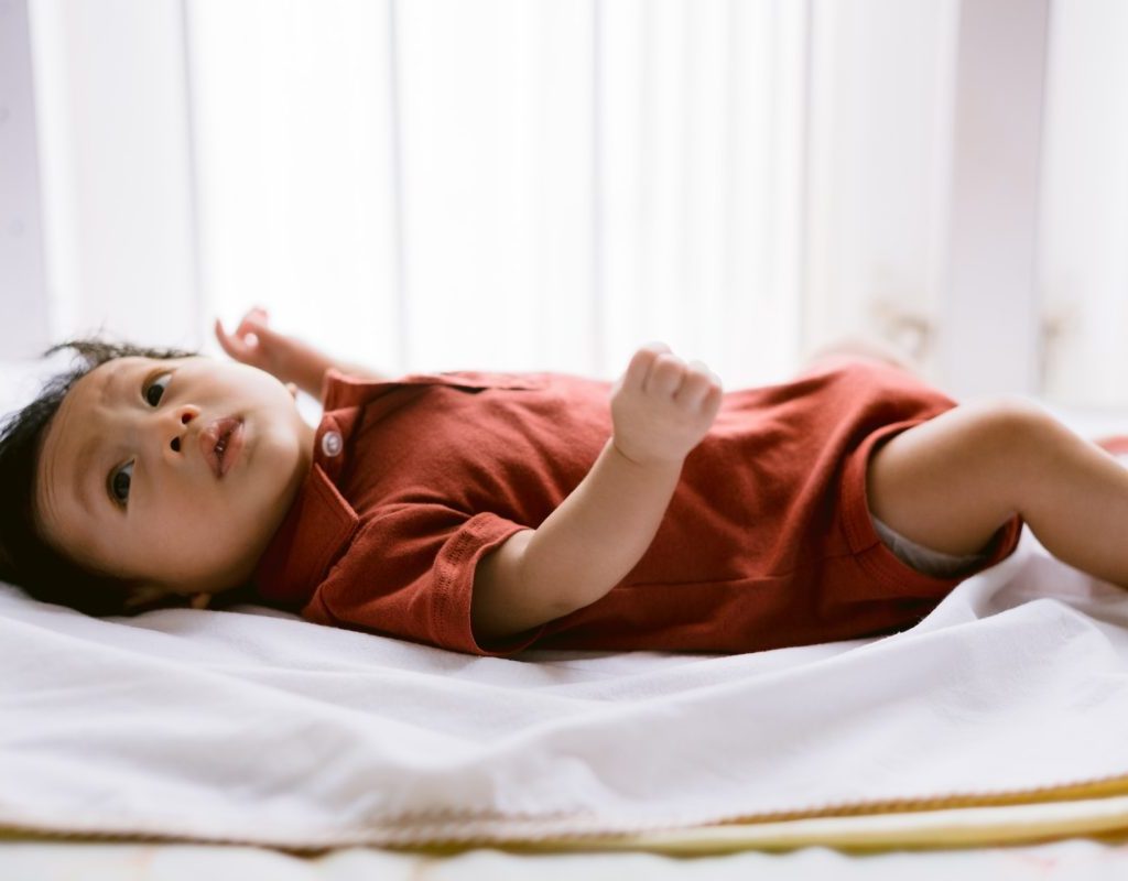A baby laying down on a bed while still awake.