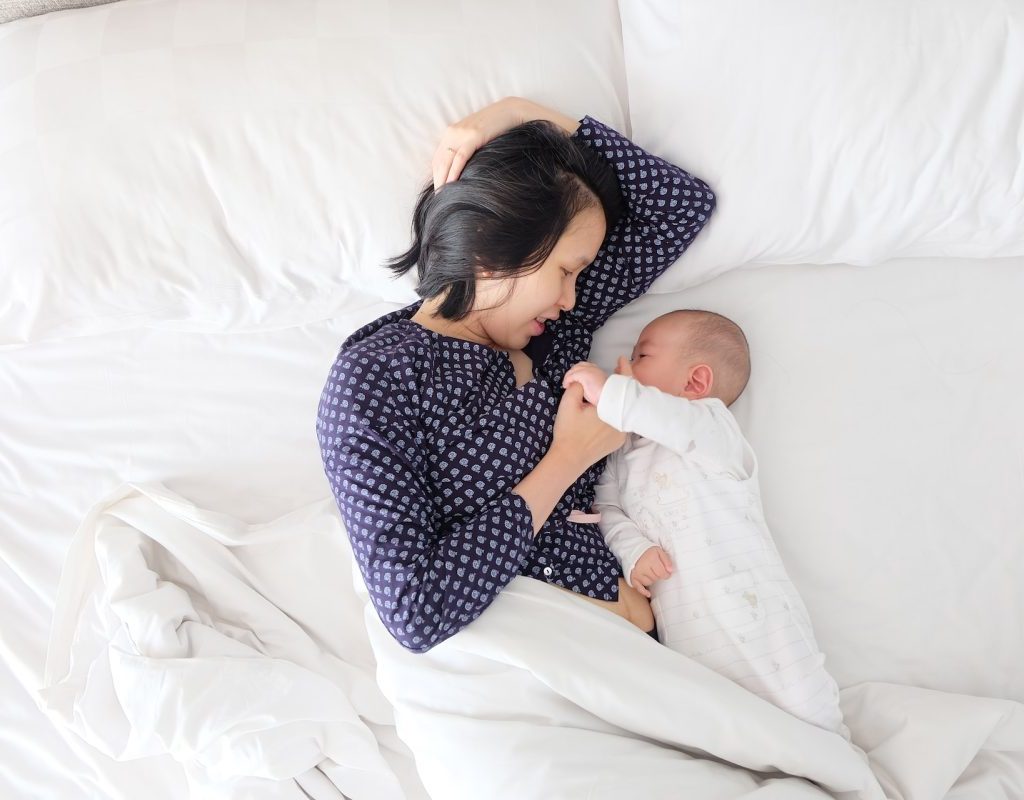 A mother and baby facing each other in the bed.