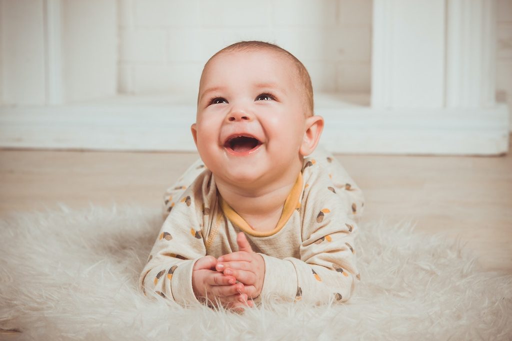A baby smiling on a white rug