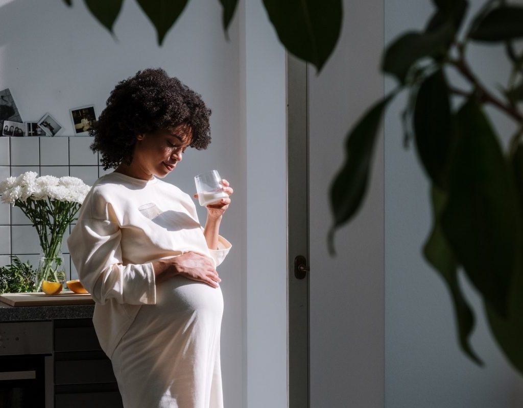 A pregnant woman holding her belly and a glass of water.