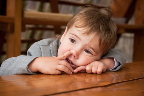 Child picking his nose while lying his head on a table