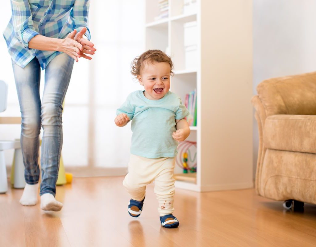 happy toddler boy running with mom following behind