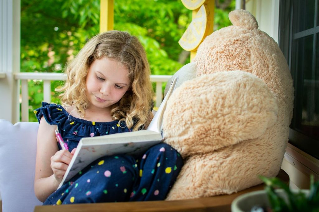Cute little girls writing in her journal with her teddy bear