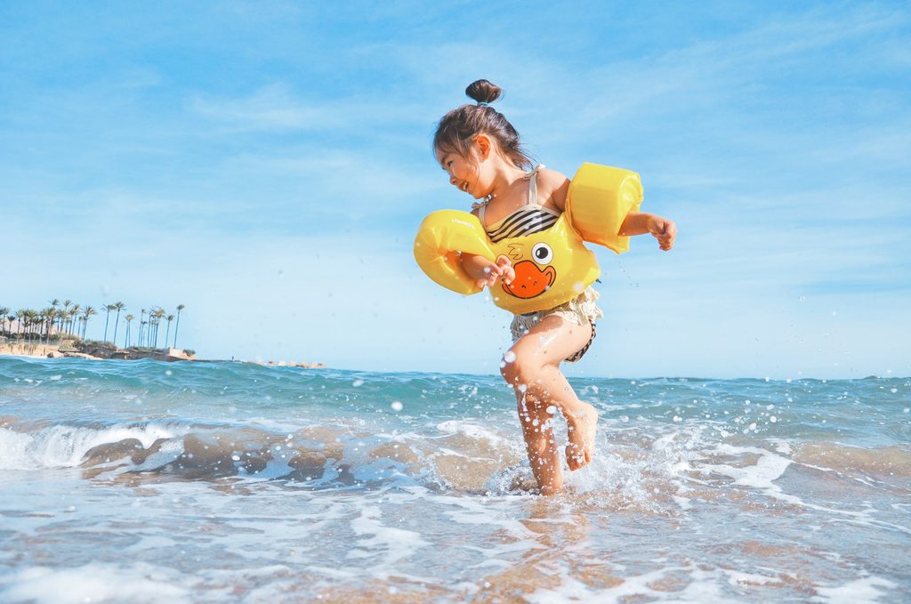 A child running in the water wearing arm floaties.