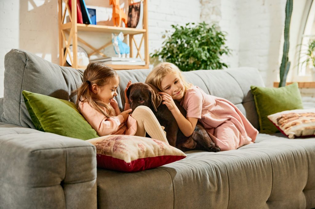 Two girls on a couch with a Labrador retriever