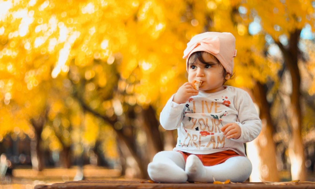 Cute baby girl sitting outside on a fall day eating snack.