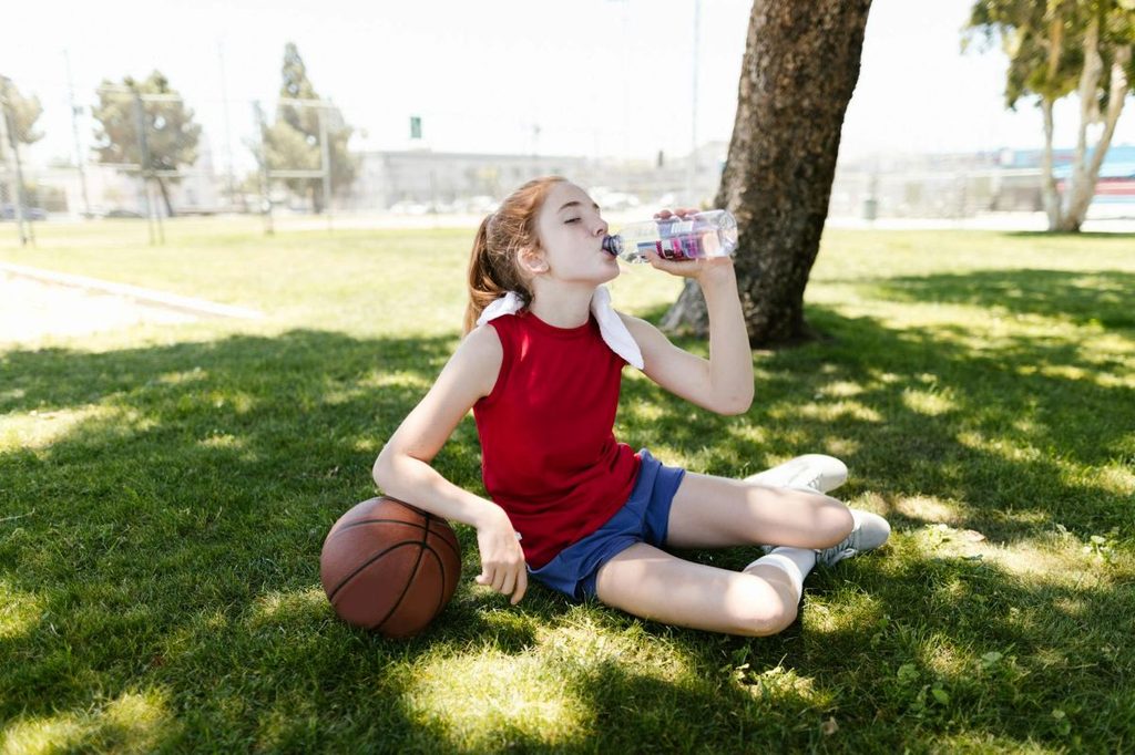 girl drinking water in the shade after basketball practice