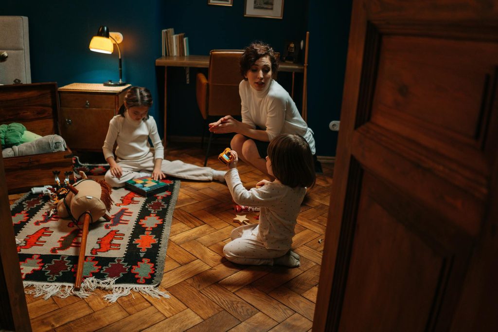 A parent talking to two children in their room while they play.