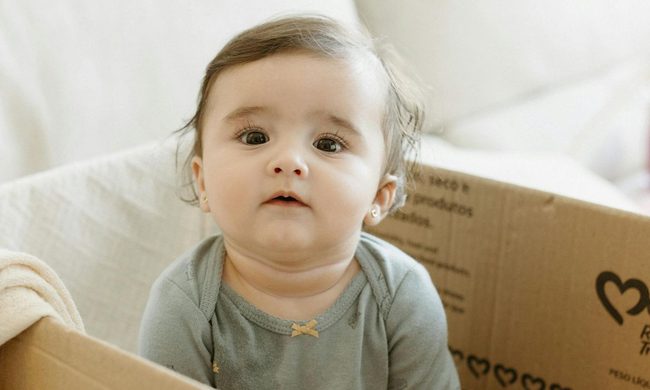 cute baby sitting in a box with pierced ears