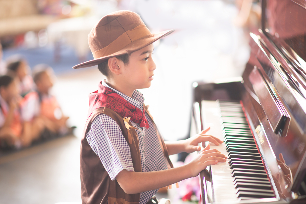 Young boys playing the piano in a talent show wearing a cowboy costume