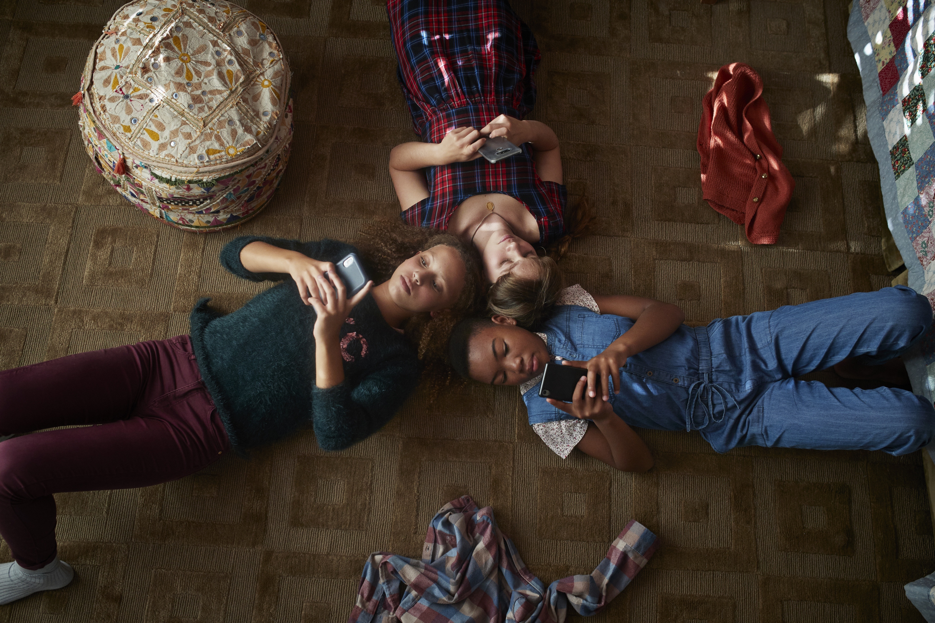 Top view of 3 tween girls looking at their smartphones