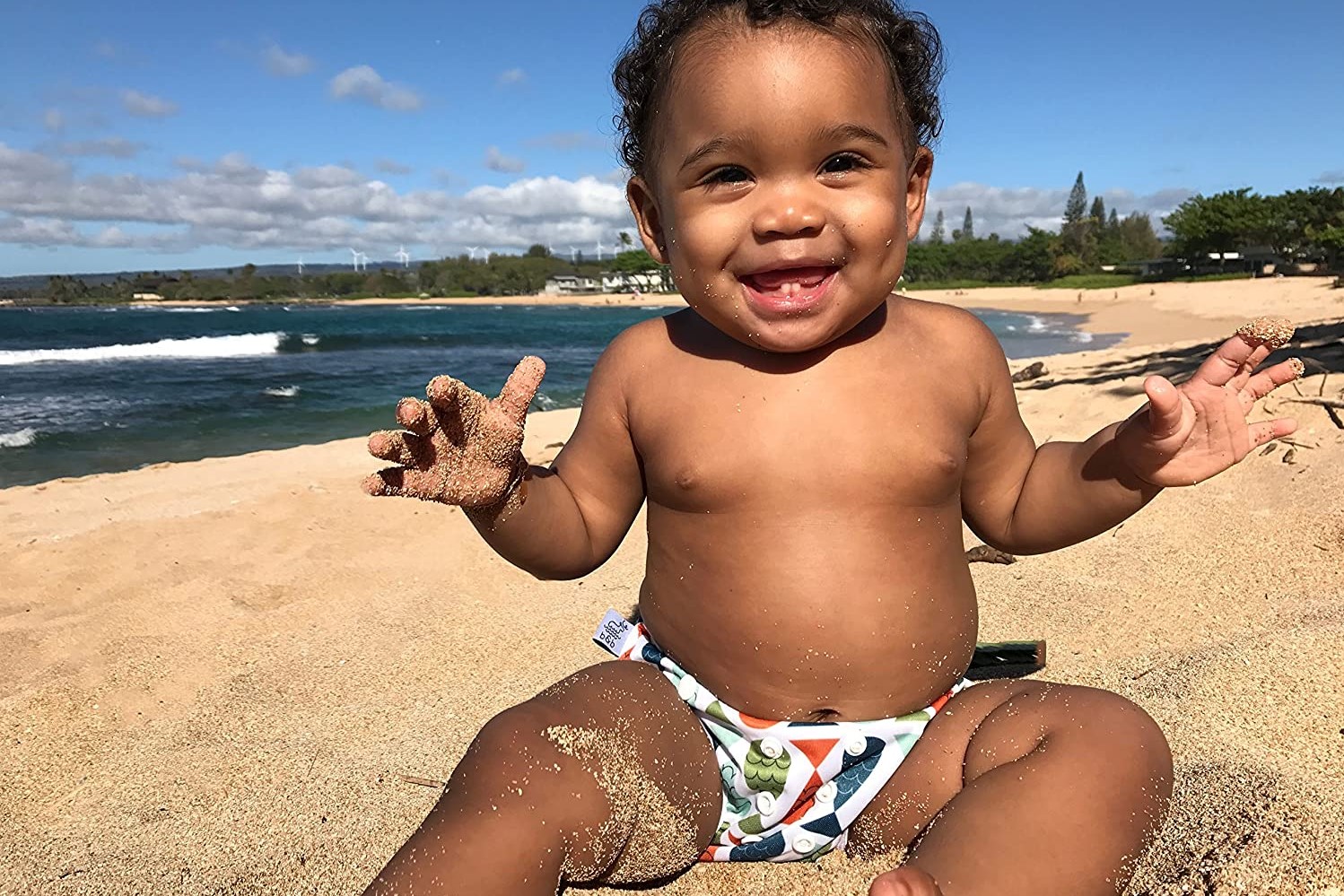 Laughing baby on beach in swim diaper
