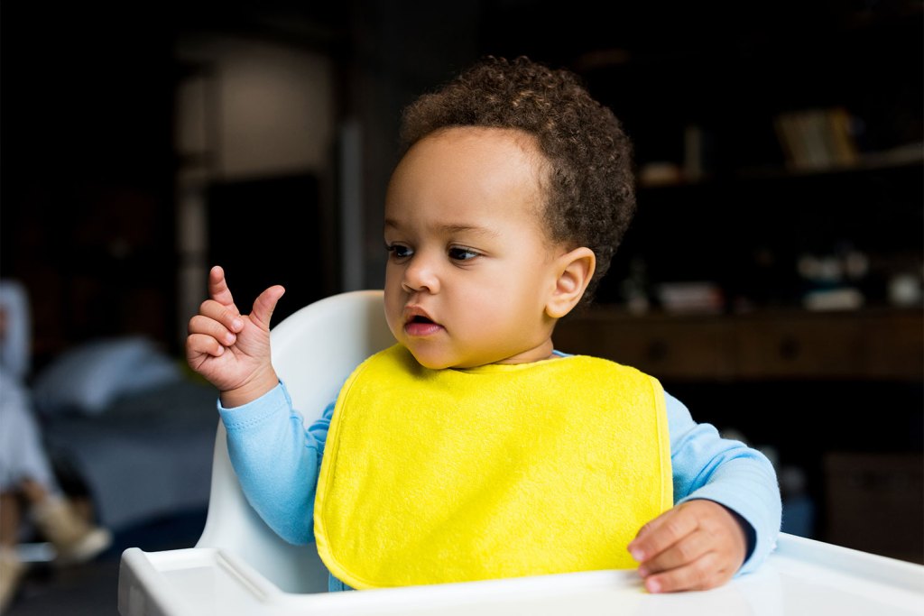 A young child wearing a bib sitting in a high chair.