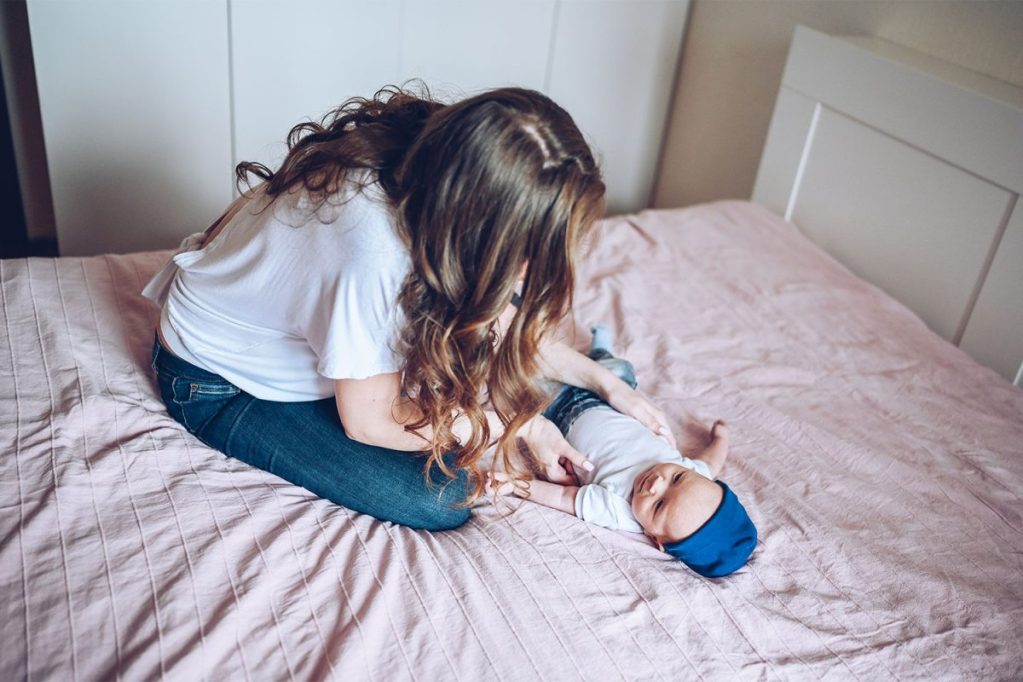 A mother changing a baby on a bed.