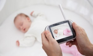 Hands holding baby monitor over crib with sleeping baby in it.