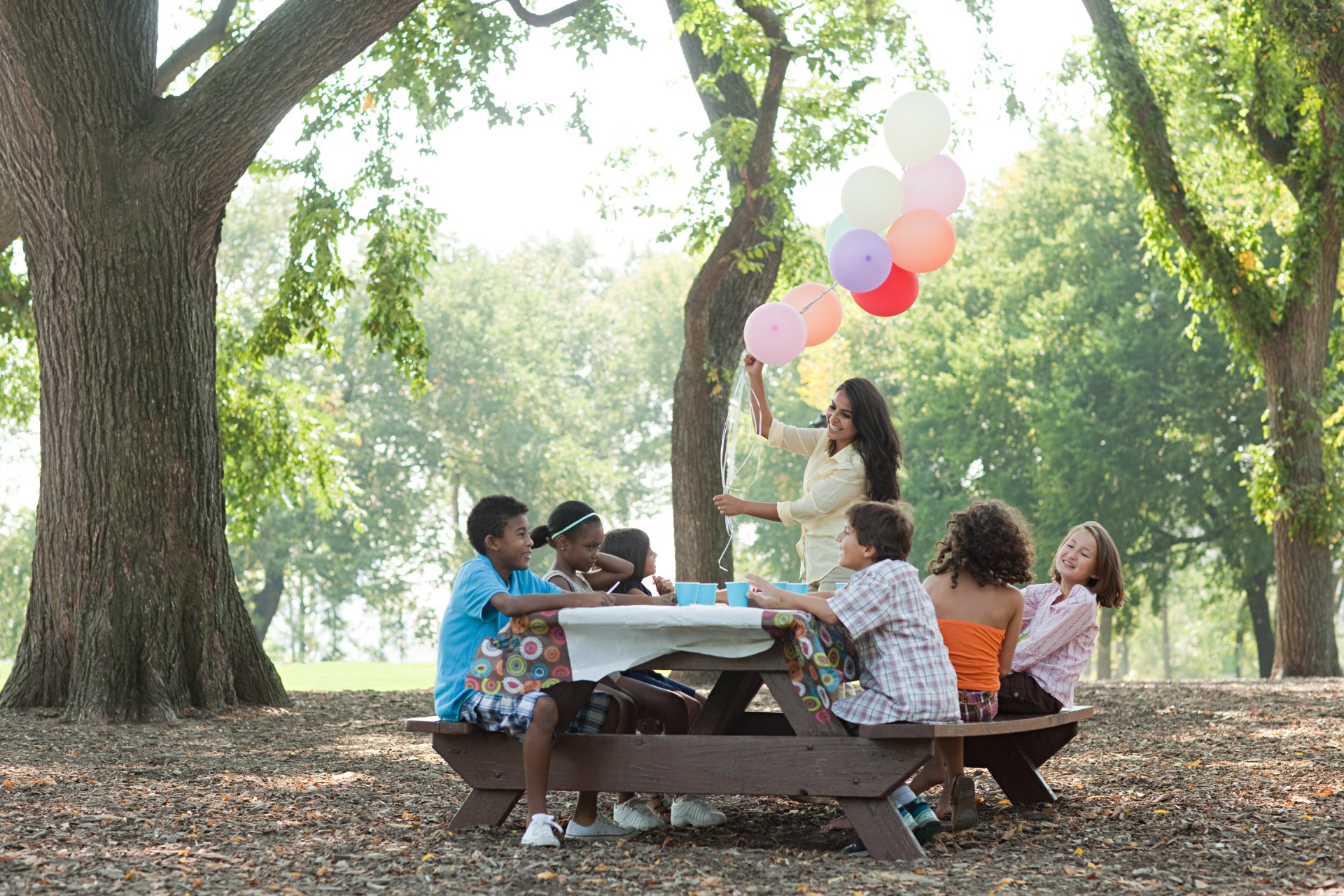 Young kids sitting at an outdoor table for a party with balloons