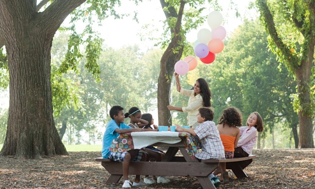 Young kids sitting at an outdoor table for a party with balloons