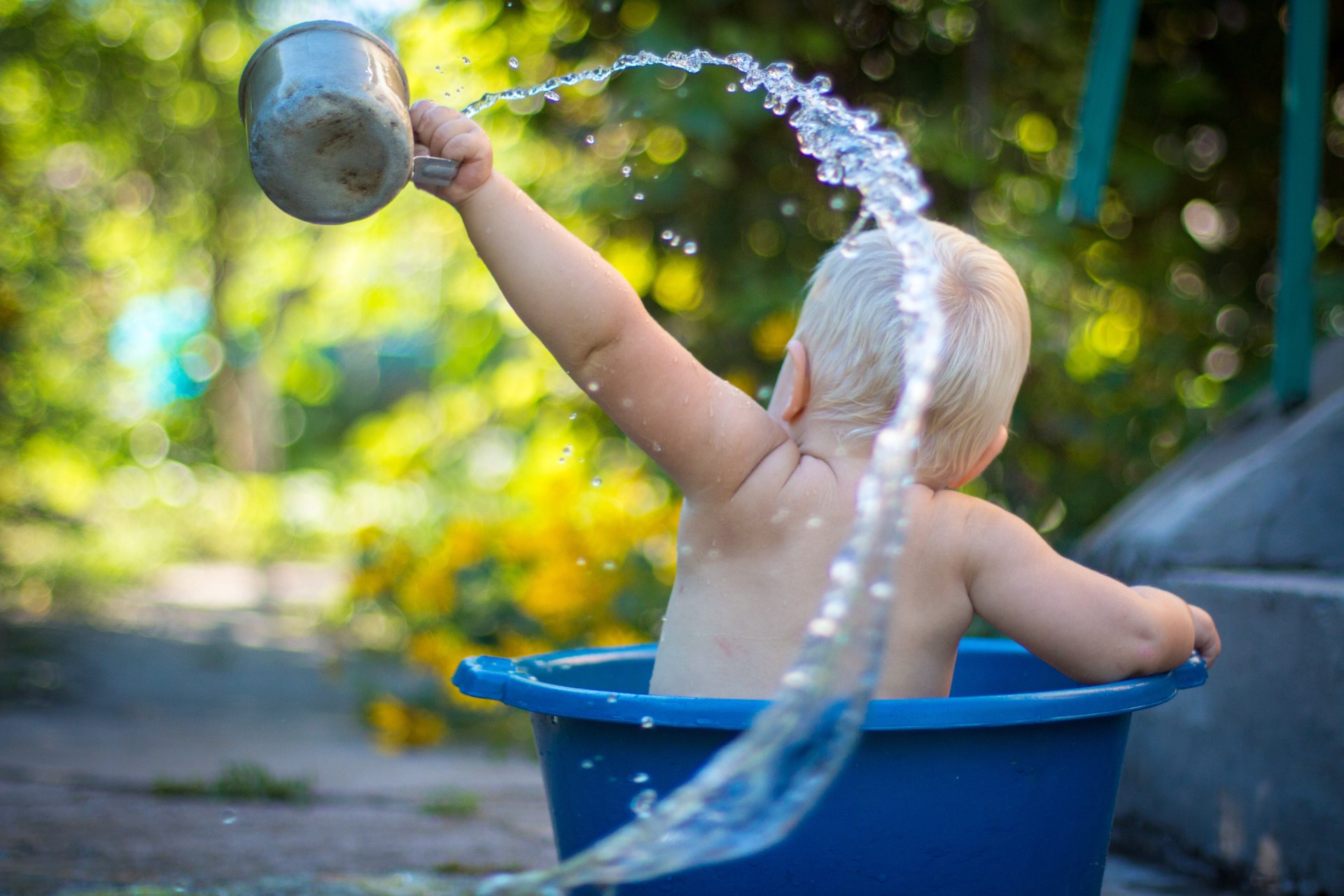 Toddler in big plastic bucket splashing water