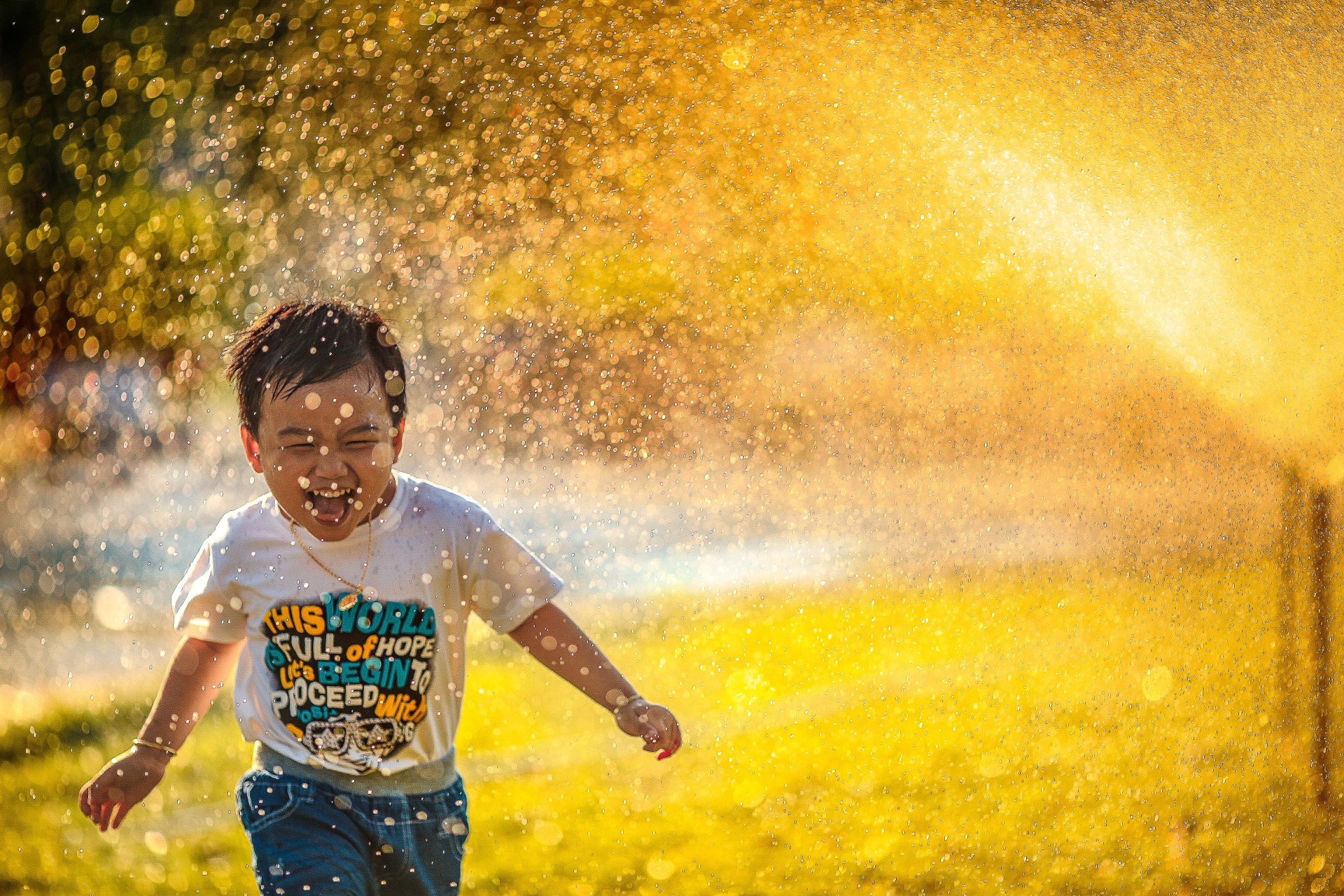 Toddler on lawn running past sprinkler