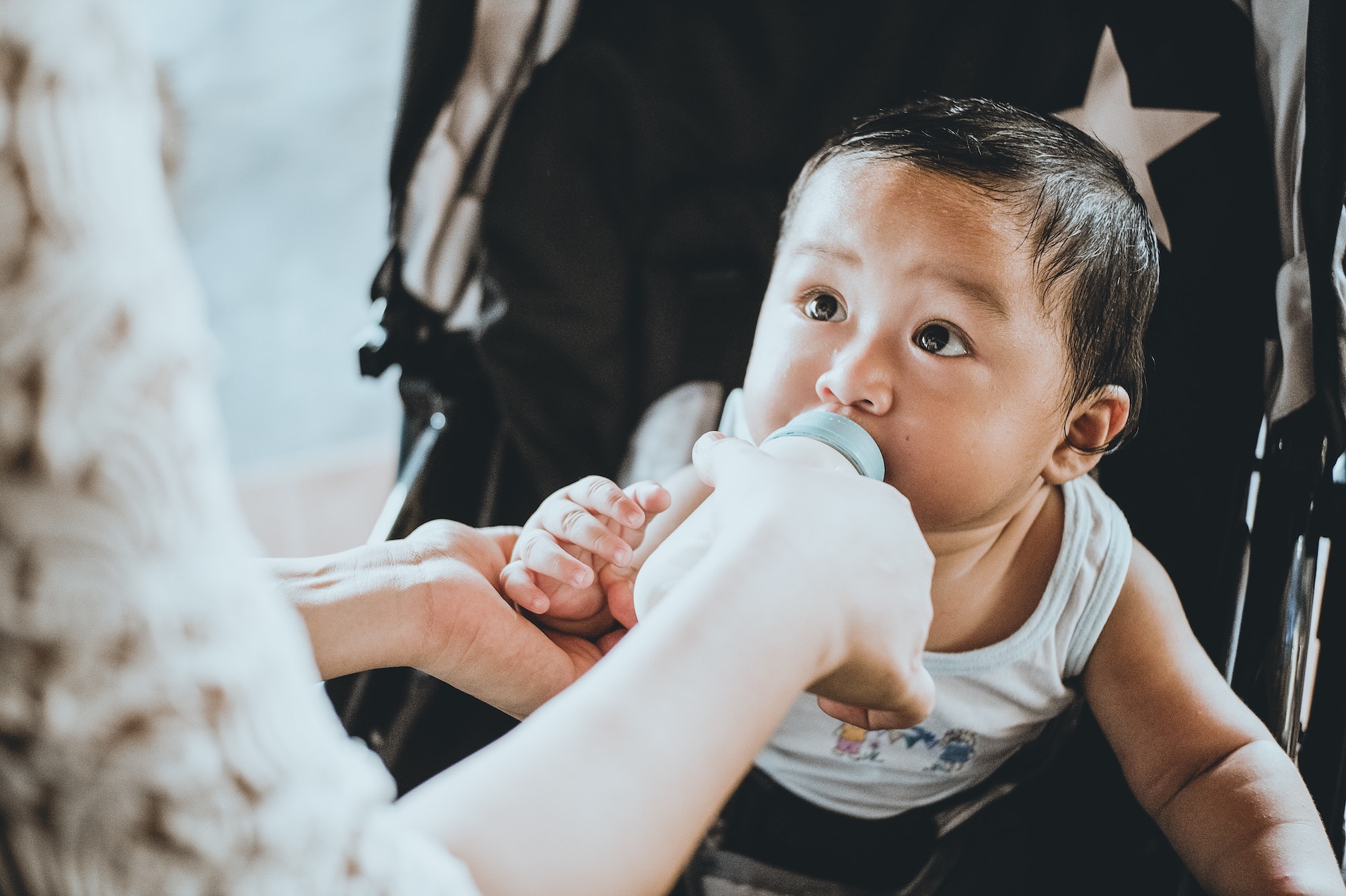Mother feeding baby with bottle in stroller.