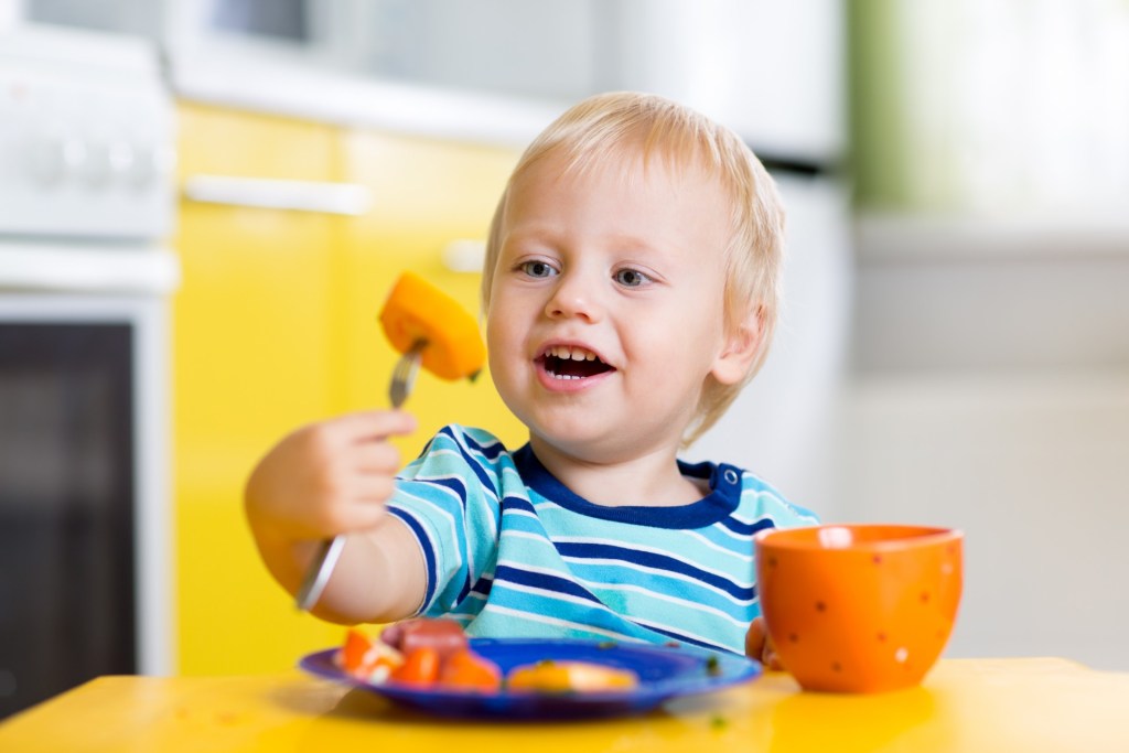 Smiling toddler at the table eating.