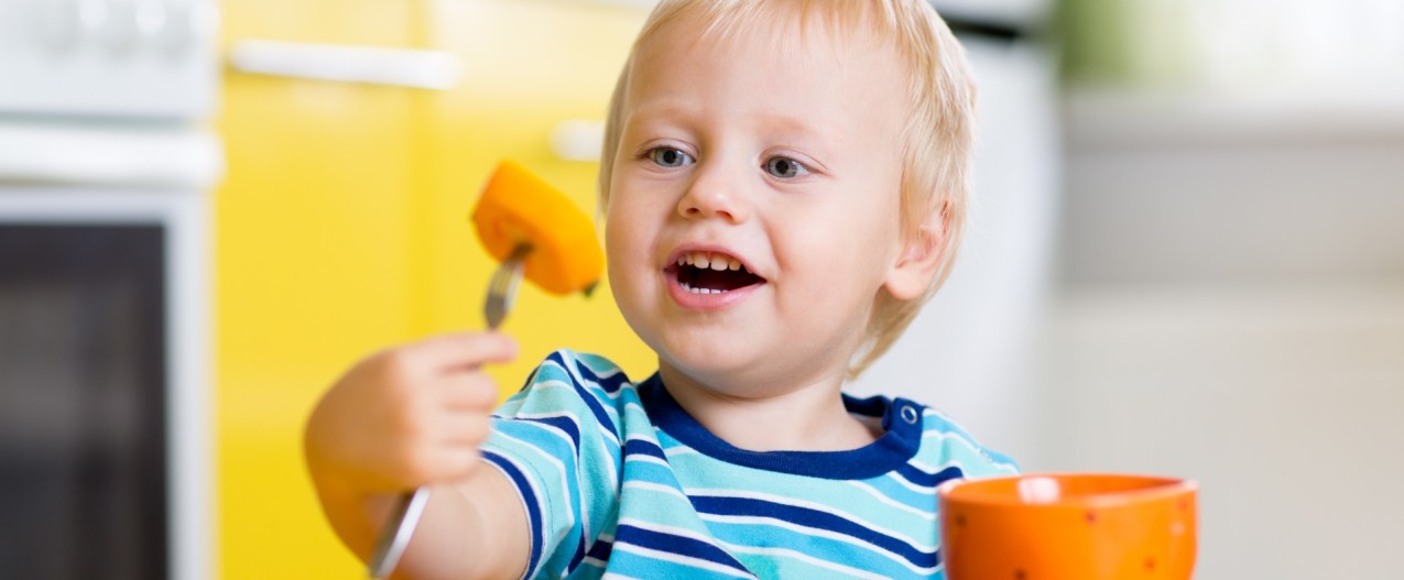 Smiling toddler at the table eating.