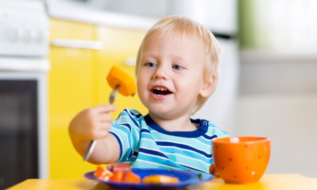 Smiling toddler at the table eating.