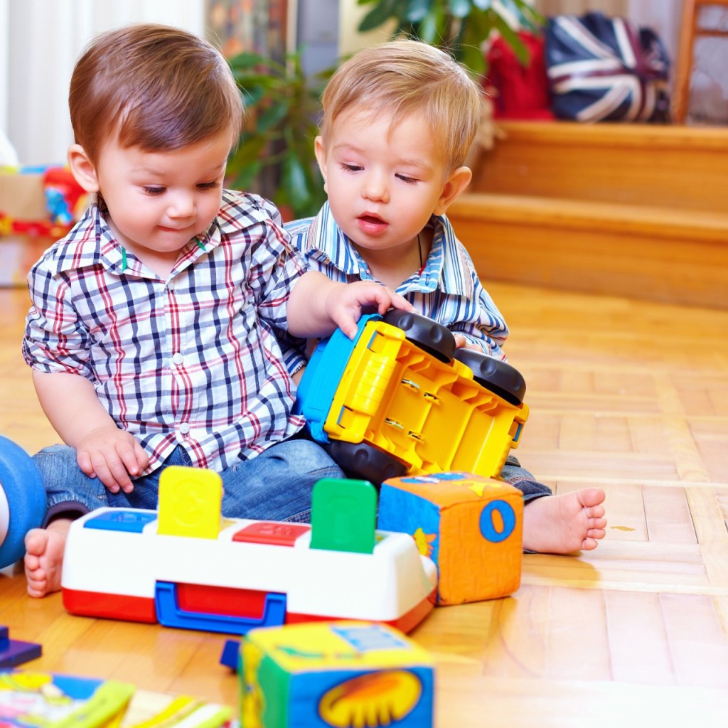 Two toddlers playing with toys on the floor