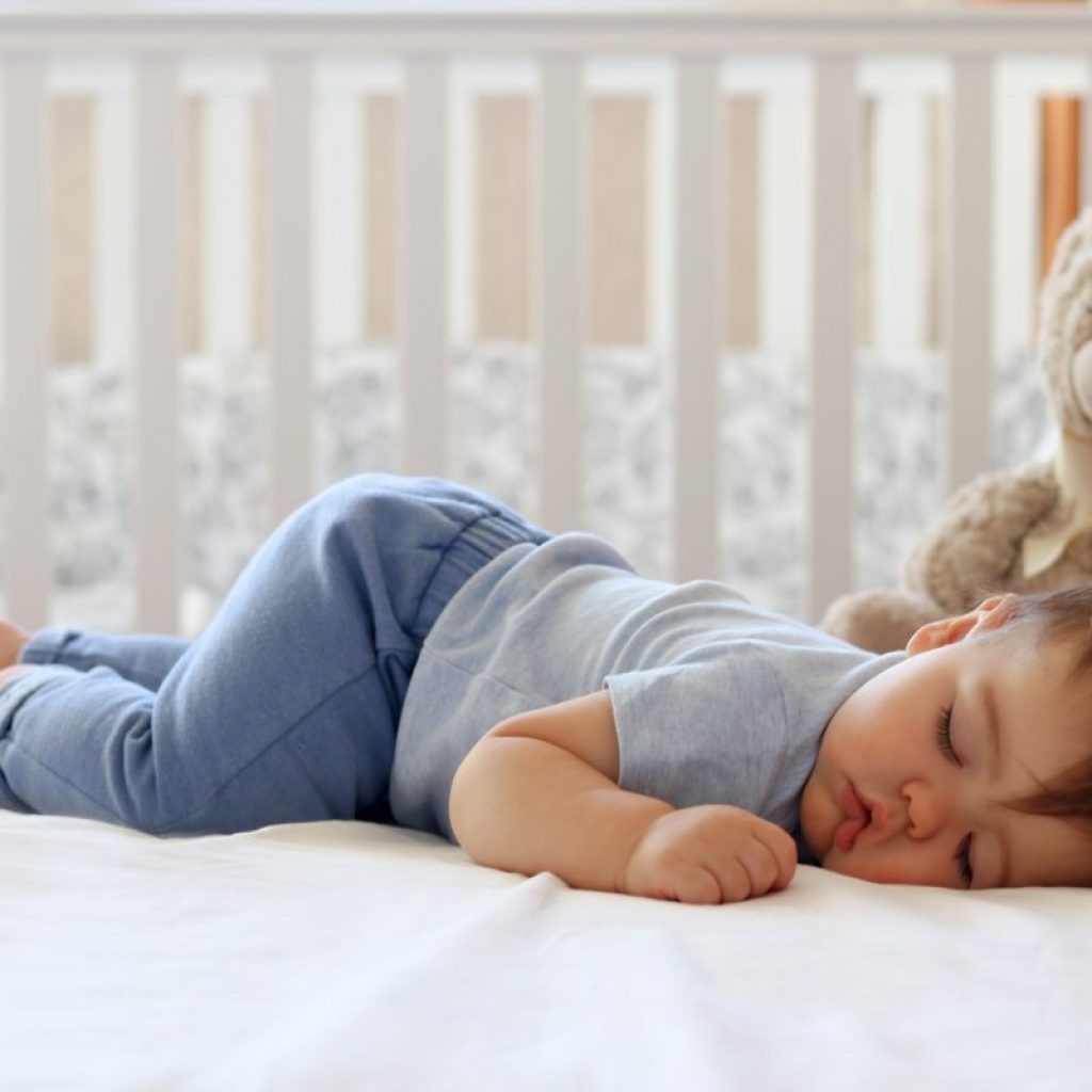 Baby sleeping in their crib with a stuffed bear.
