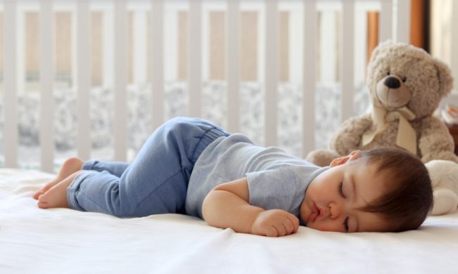 Baby sleeping in their crib with a stuffed bear