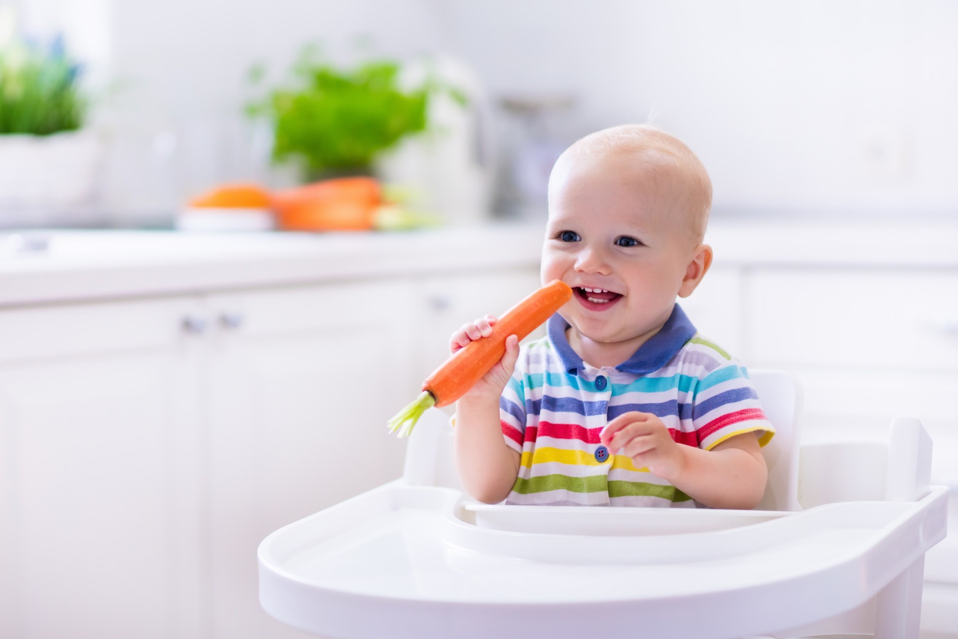 Smiling baby in high chair holding a carrot