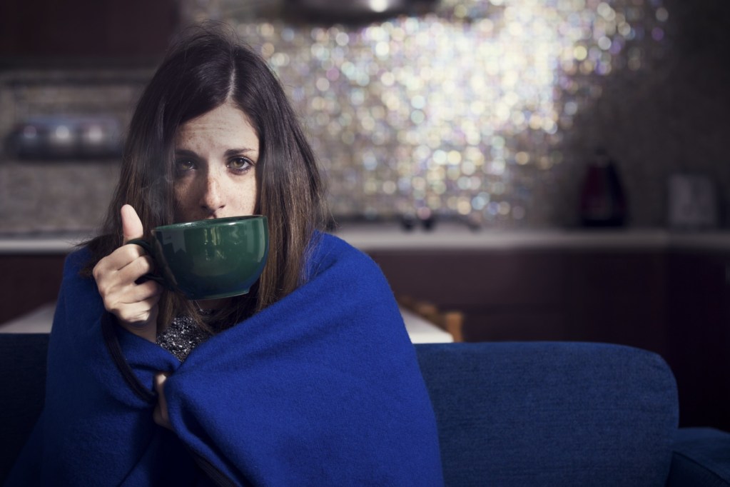 Woman in blanket drinking cold medicine