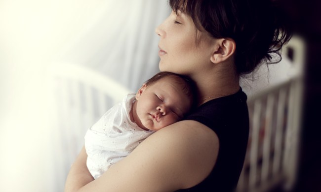Mother holding a sleeping baby near a crib