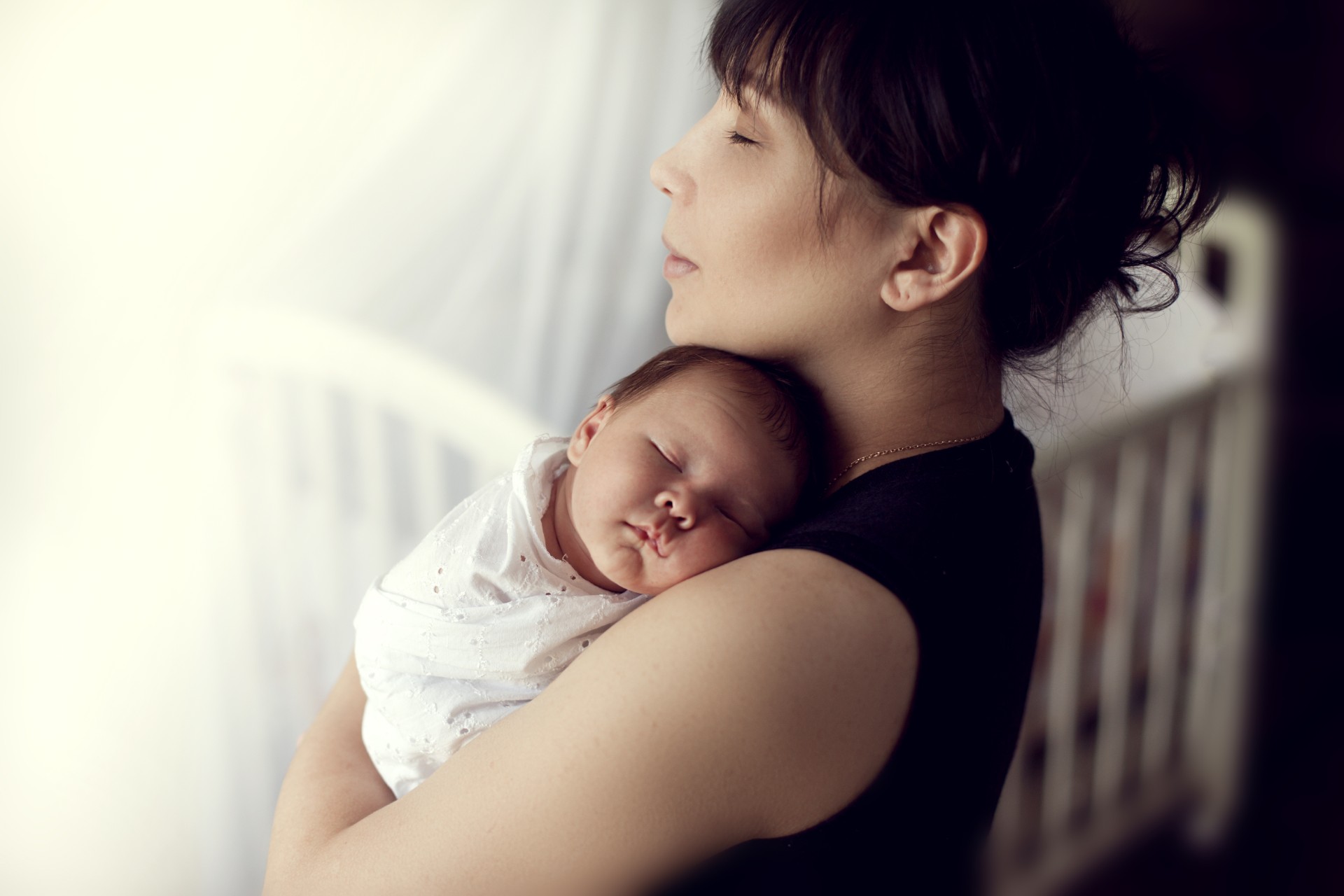 Mother holding a sleeping baby near a crib
