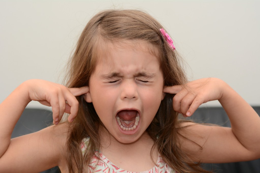 Young girl is screaming with fingers in her ears.